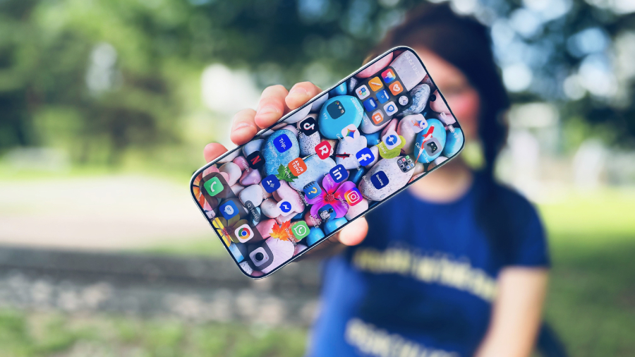 Žena drží v ruce rozsvícený mobilní telefon HONOR 600 Pro s mnoha aplikacemi na barevné tapetě v rozostřeném venkovním parku.