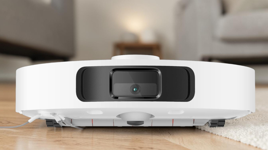 Detailní čelní pohled na kameru a senzory bílého robotického vysavače Xiaomi Robot Vacuum X20+, který stojí na přechodu mezi dřevěnou podlahou a světlým kobercem.