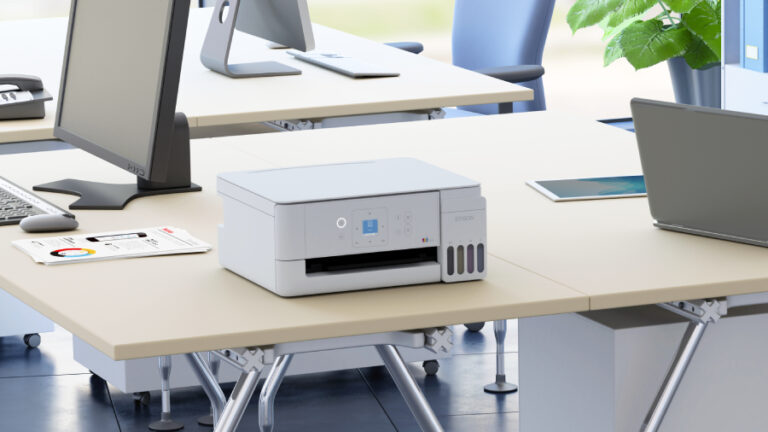 Bílá multifunkční inkoustová tiskárna Epson EcoTank L3366 v bílém provedení umístěná na světlém kancelářském stole v moderním společném pracovním prostoru.