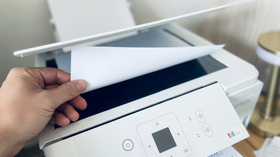 Ruka vkládající čistý bílý list papíru na skleněnou plochu skeneru pod odklopené víko tiskárny Epson EcoTank L3366.