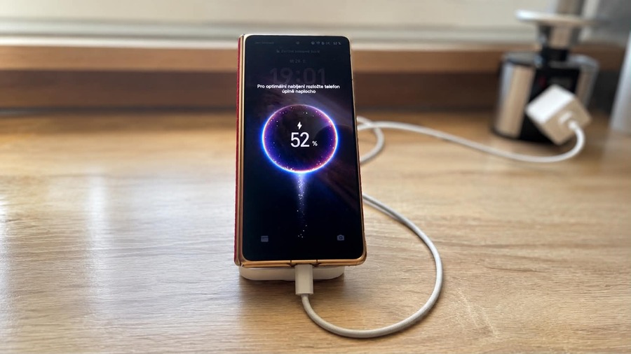 Skládací telefon HONOR Magic V6 stojící v stojánka a připojený k nabíječce s rozsvíceným displejem zobrazujícím probíhající nabíjení na 52 %.
