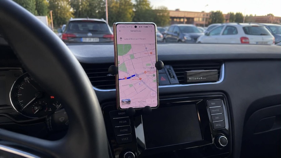 Skládací telefon HONOR Magic V6 uchycený v držáku na palubní desce auta, na jehož rozsvíceném displeji běží navigační aplikace s mapou.