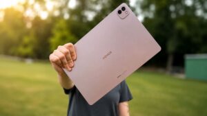 Detailní záběr na zadní stranu tabletu HONOR MagicPad 4, který drží člověk před sebou. Pozadí tvoří rozostřená, sluncem zalitá zahrada.