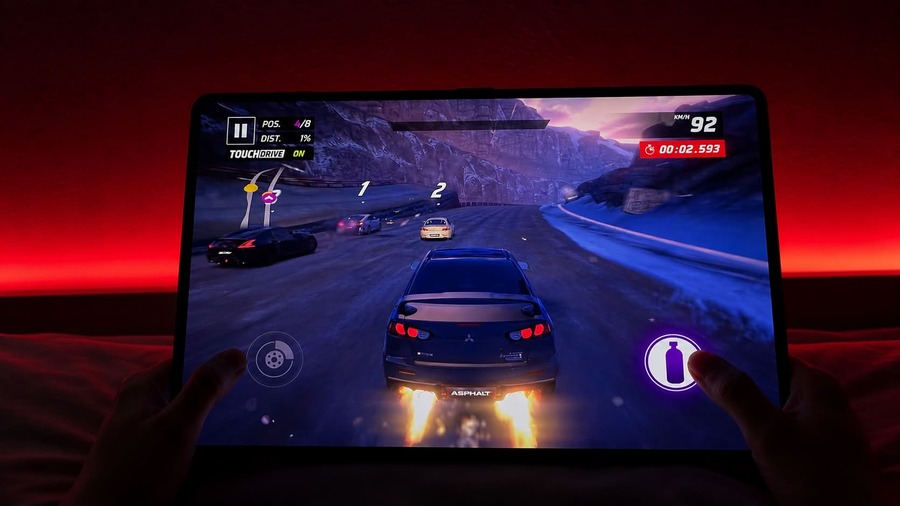 Detailní záběr tabletu HONOR MagicPad 4, na kterém hráč hraje závodní hru Asphalt v tmavé místnosti s výrazným červeným podsvícením.