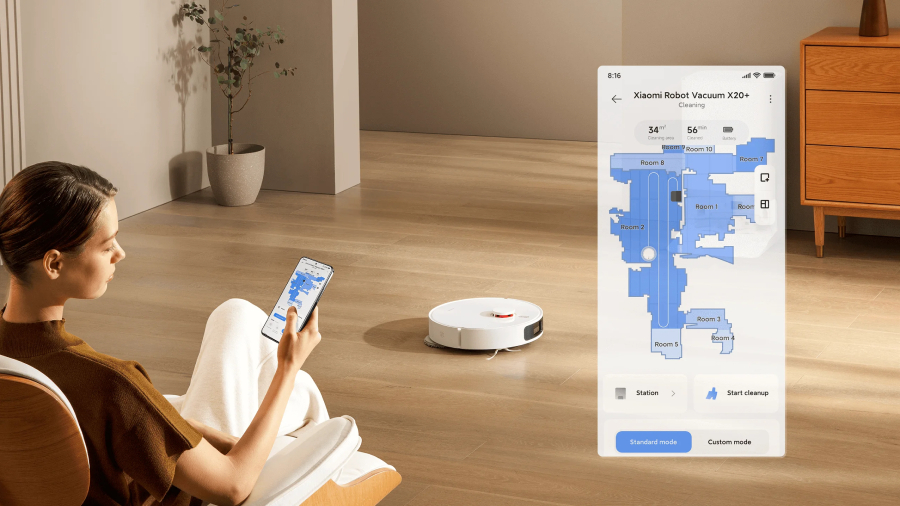 Žena sedí v křesle a na chytrém telefonu ovládá robotický vysavač Xiaomi Robot Vacuum X20+, přičemž grafika vedle ní detailně zobrazuje digitální mapu místností v aplikaci Mi Home.