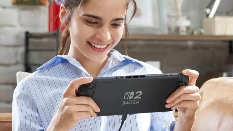 Usmívající se žena držící v rukou konzoli Nintendo Switch 2 v kapesním režimu, která je připojena k nabíjecímu kabelu.