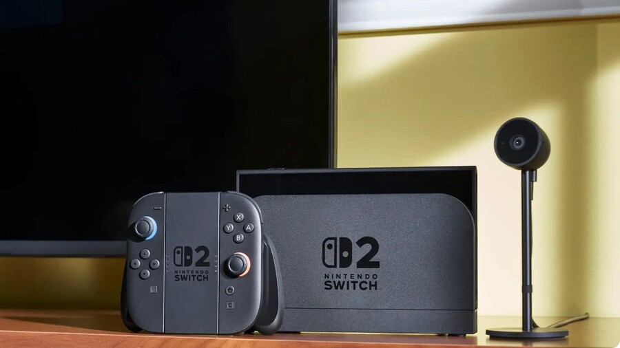 Herní konzole Nintendo Switch 2 v dokovací stanici spolu s ovladačem a kamerou na polici před televizorem.