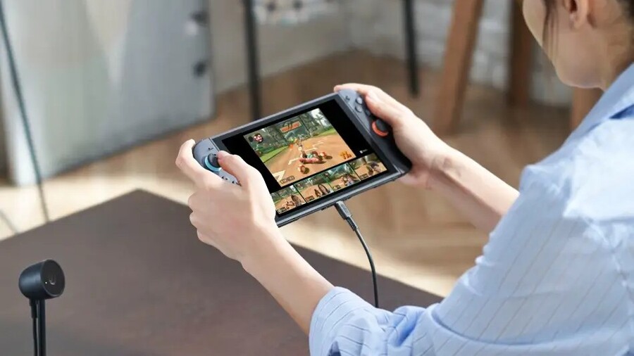 Člověk držící konzoli Nintendo Switch 2, která je v průběhu hraní připojena k napájecímu kabelu.