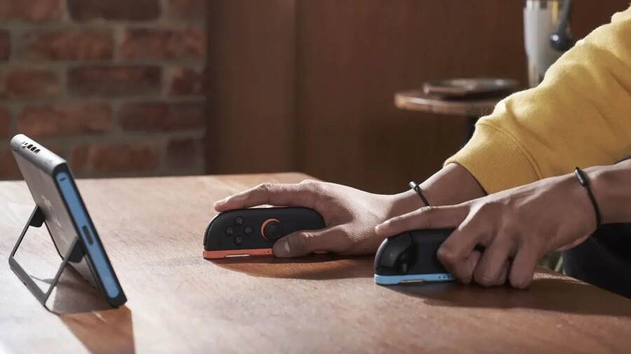 Člověk hrající na konzoli Nintendo Switch 2 umístěné na stojánku, přičemž používá odpojené ovladače položené samostatně na stole.