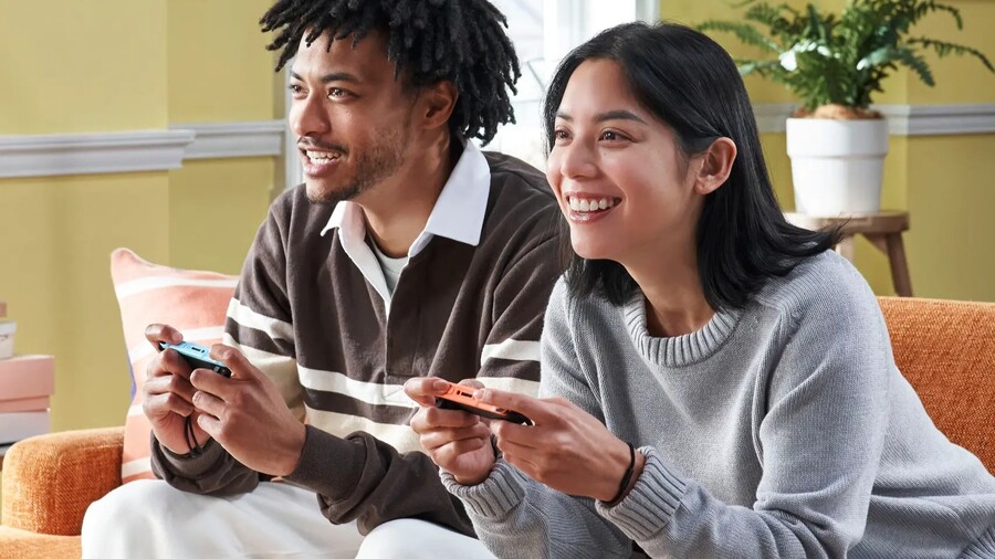 Mladý pár se usmívá a společně hraje videohry na ovladačích Nintendo Switch 2 v obývacím pokoji.
