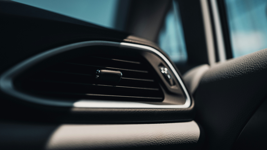 Detailní záběr na uzavřený, černý plastový větrací otvor (výdech klimatizace) v moderním automobilu, zvýrazněný stříbrným lemováním.