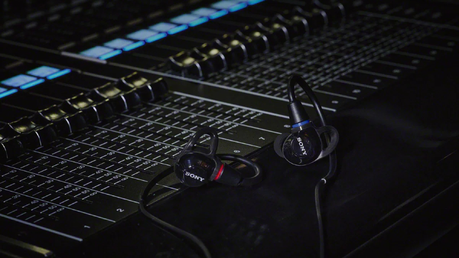 Černá verze in-ear monitorů Sony IER-M500 položená na profesionálním mixážním pultu ve tmavém studiu.