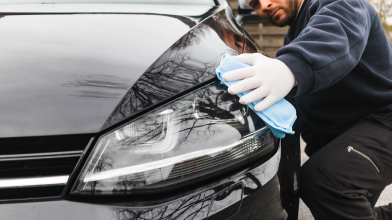 Muž v rukavicích čistí mikrovláknovou utěrkou světlomet černého osobního automobilu.