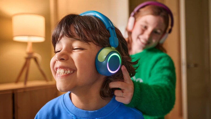 Back to school: Usmívající se chlapec s modro-zelenými svítícími sluchátky Philips TAK4200, kterých se zezadu dotýká ruka dívky s fialovými sluchátky Philips.