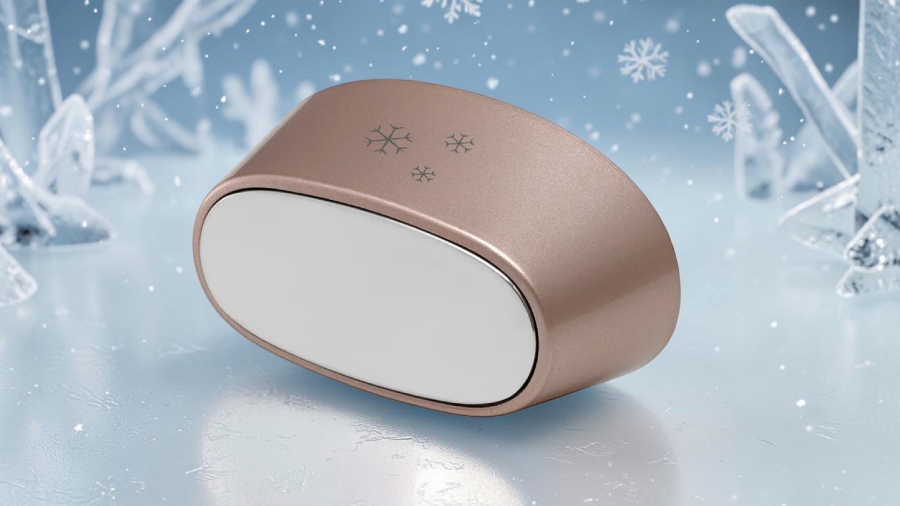 Detailní pohled na oválný chladicí nástavec v barvě taupegold se třemi vločkami a stříbrnou kovovou aplikační plochou k epilátoru Concept Perfect Skin PRO anti age IL5020, který leží na modrém zamrzlém ledovém podkladu s padajícím sněhem.