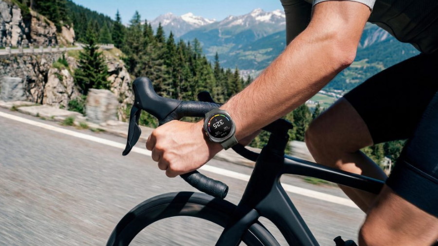 Detailní záběr na ruku cyklisty držícího řidítka silničního kola v přírodě s chytrými hodinkami Galaxy Watch Ultra2 na zápěstí.