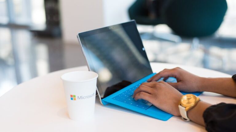 Uživatel pracující na notebooku s Windows a Microsoft Office u stolu s kelímkem Microsoft.