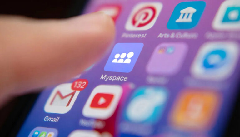 Detailní pohled na prst dotýkající se obrazovky chytrého telefonu, kde svítí ikona aplikace Myspace obklopená dalšími platformami jako Gmail, YouTube nebo Pinterest.