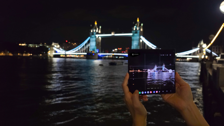 Pohled na ruce fotografující osvětlený most Tower Bridge v Londýně pomocí rozloženého vnitřního displeje chytrého telefonu Samsung Galaxy Z Fold8 Ultra během nočního testování.