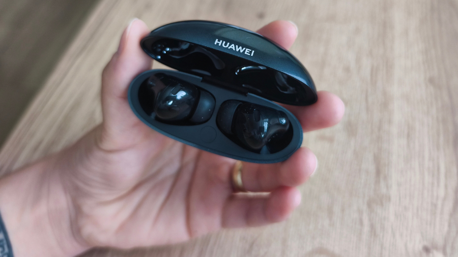 Otevřené černé nabíjecí pouzdro se sluchátky Huawei FreeBuds Neo v dlaních.