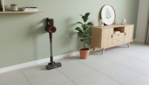 Tyčový vysavač JIGOO C200 Cordless Vacuum Cleaner stojí volně opřený o světle zelenou zeď v moderním pokoji s kachlovou podlahou.