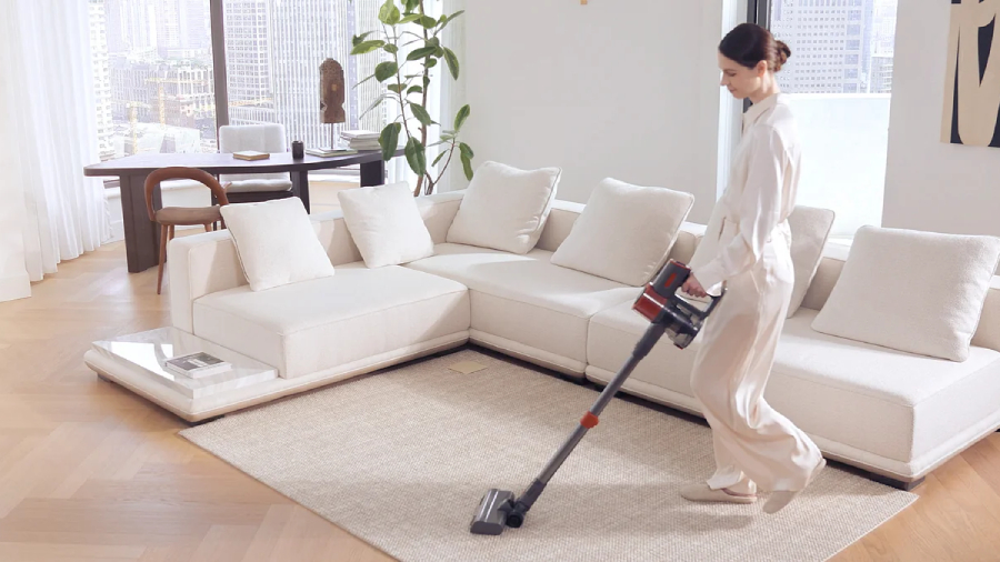 Žena v bílém oblečení vysává světlý koberec v moderním obývacím pokoji pomocí tyčového vysavače JIGOO C200 Cordless Vacuum Cleaner.
