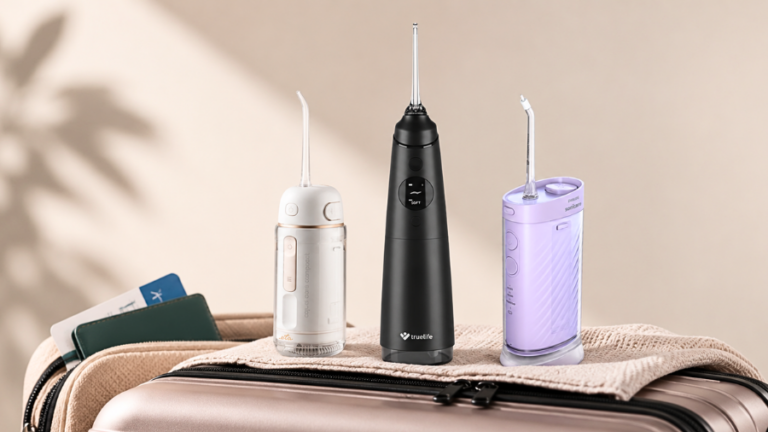 Tři kompaktní ústní sprchy ETA, TrueLife a Philips Sonicare položené na cestovním kufru.