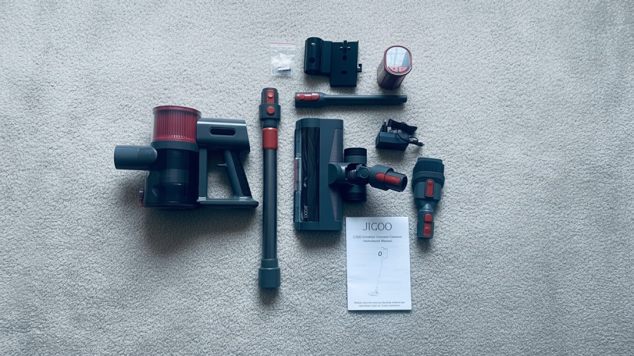 Kompletní příslušenství a díly tyčového vysavače JIGOO C200 Cordless Vacuum Cleaner rozložené na světlém koberci včetně manuálu.