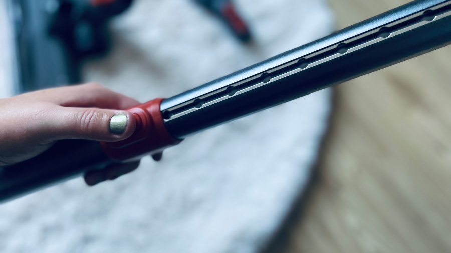 Detailní pohled na stisknutí červeného tlačítka při nastavování délky kovové teleskopické trubice vysavače JIGOO C200 Cordless Vacuum Cleaner.