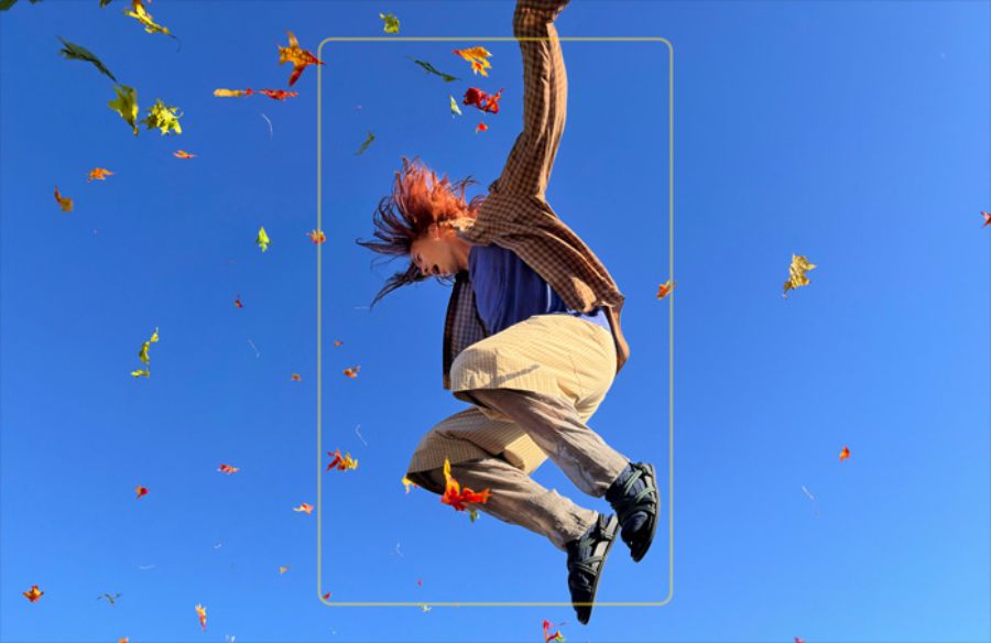 Dynamický akční záběr z fotoaparátu na skládacím telefonu iPhone Duo, který zachycuje ženu skákající vysoko do vzduchu proti jasně modré obloze mezi padajícím podzimním listím.